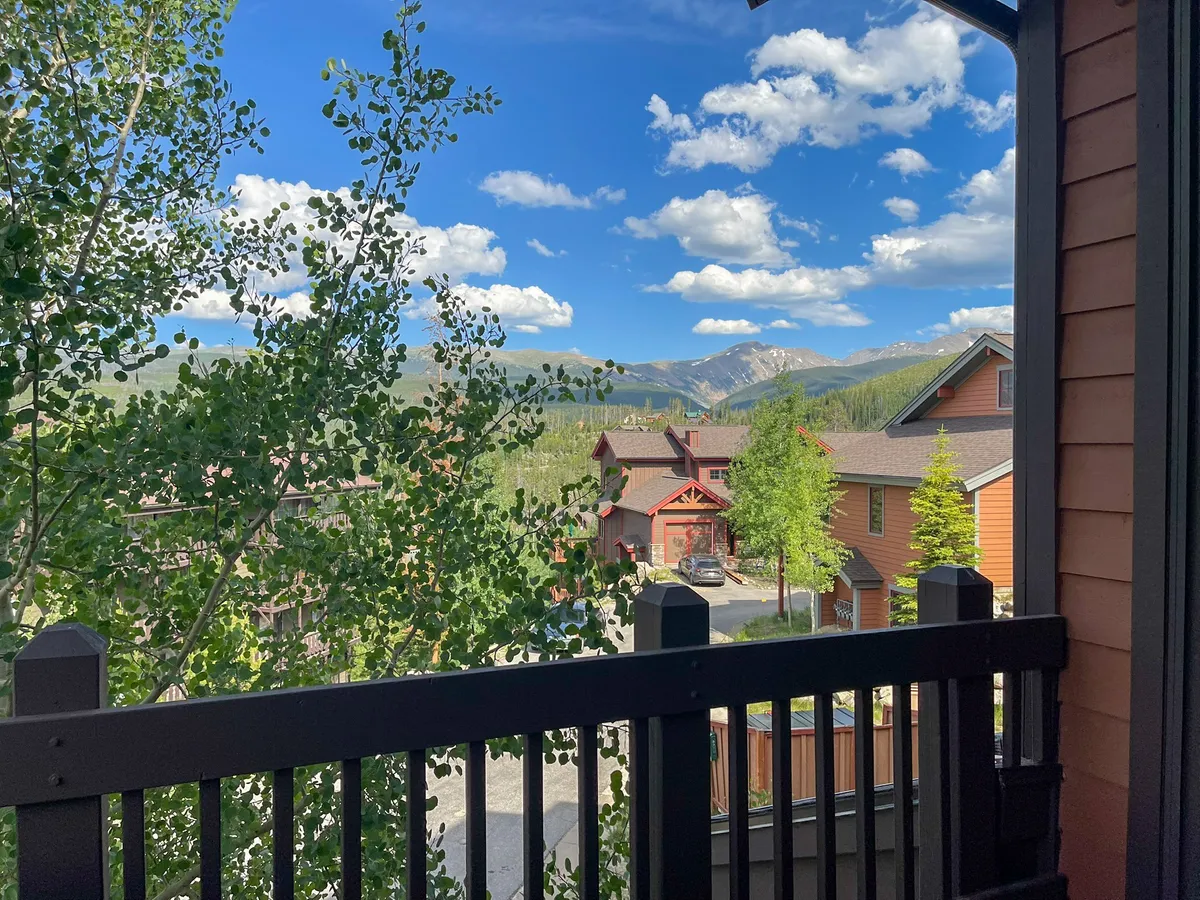 A panoramic view of the surrounding mountain range under a bright blue sky, framed by foreground trees and buildings. This tranquil scene evokes the vastness and beauty of the Colorado landscape, ideal for hiking, wildlife viewing, and unwinding after a day of adventure.