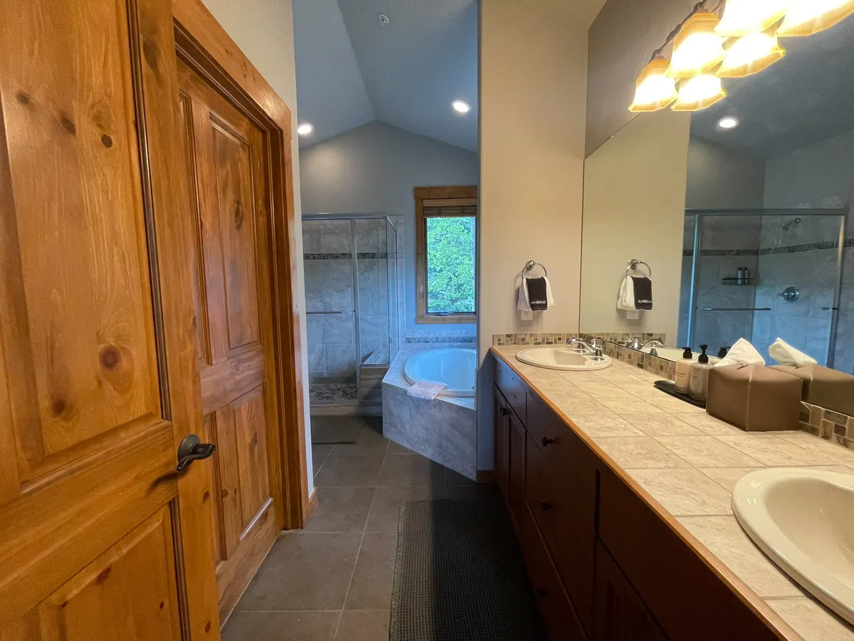 A serene, modern bathroom featuring a double vanity, bathtub, shower area, and a window that lets in natural light. The ambiance is spa-like, perfect for relaxation and renewal after outdoor activities.
