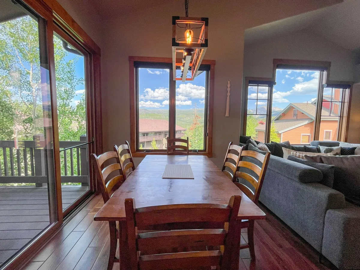 A dining area featuring a large table positioned adjacent to expansive windows, offering clear mountain views. The setting suggests versatility, perfect for family dinners, casual breakfasts, or evening board games, with natural light flooding the space.