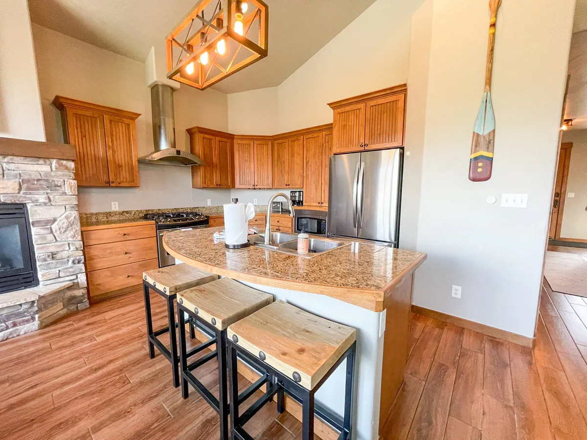 A cozy kitchen featuring a spacious island with stools, granite countertops, gleaming stainless steel appliances, and warm wooden cabinetry. The layout is open, offering plenty of workspace for meal preparation and areas for guests or family to gather nearby. The inviting atmosphere reflects an environment perfect for cooking, entertaining, and sharing meals.