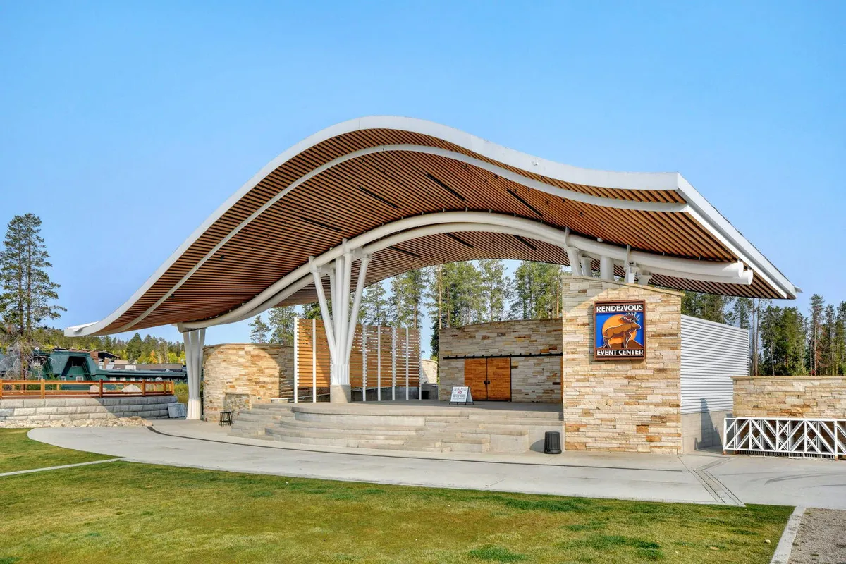 A lively outdoor venue with a curved roof, stone façade, and stage area, perfect for concerts, seasonal festivals, and community gatherings. The area is bathed in uplifting light, suggesting a vibrant, active hub nearby.
