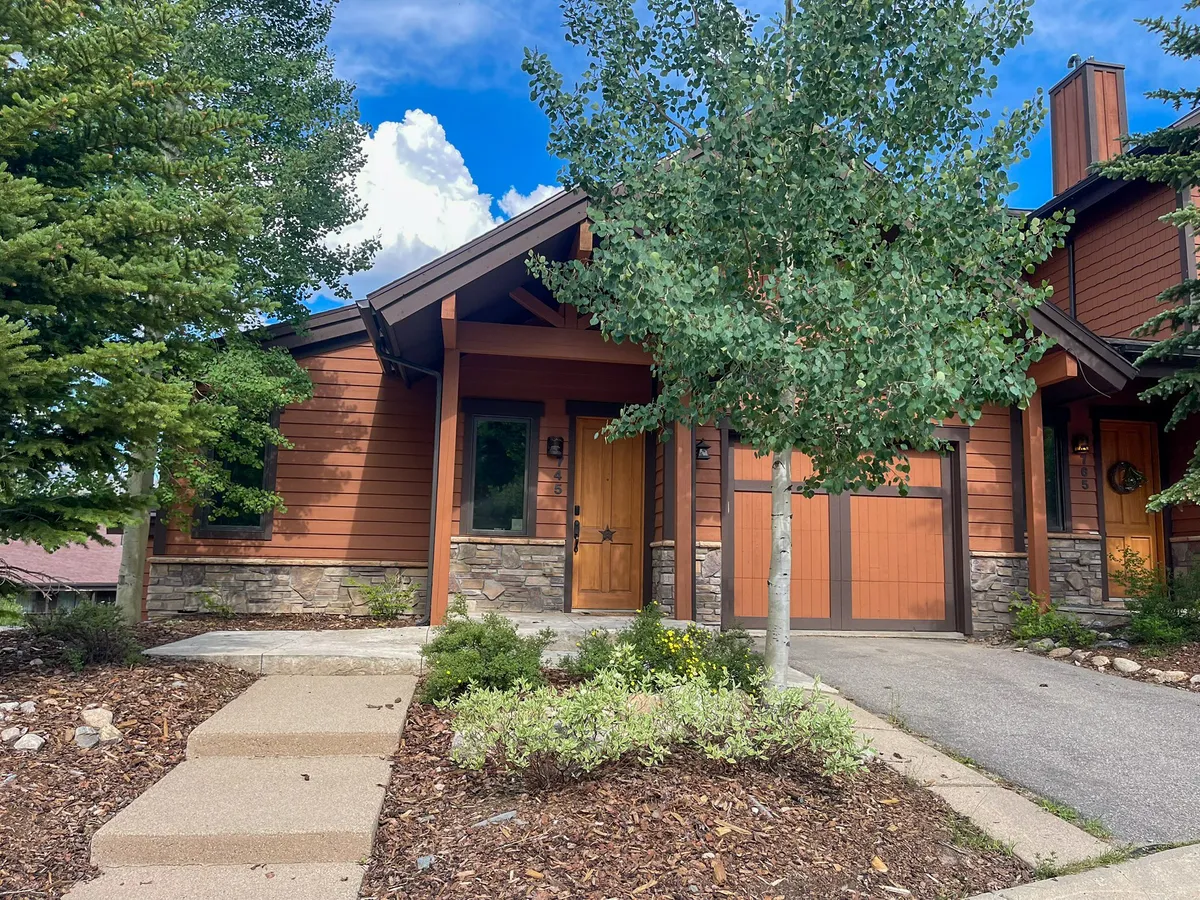 The hero image displays the elegant exterior of a luxury single-family home nestled in Winter Park, Colorado. The scene features a grand wooden door framed by rustic stone accents, a beautifully landscaped garden with lush greenery, and slender aspen trees offering a tranquil alpine vibe. The spacious porch invites guests to relax, while the surrounding natural beauty hints at peaceful mornings and unforgettable evenings outdoors.