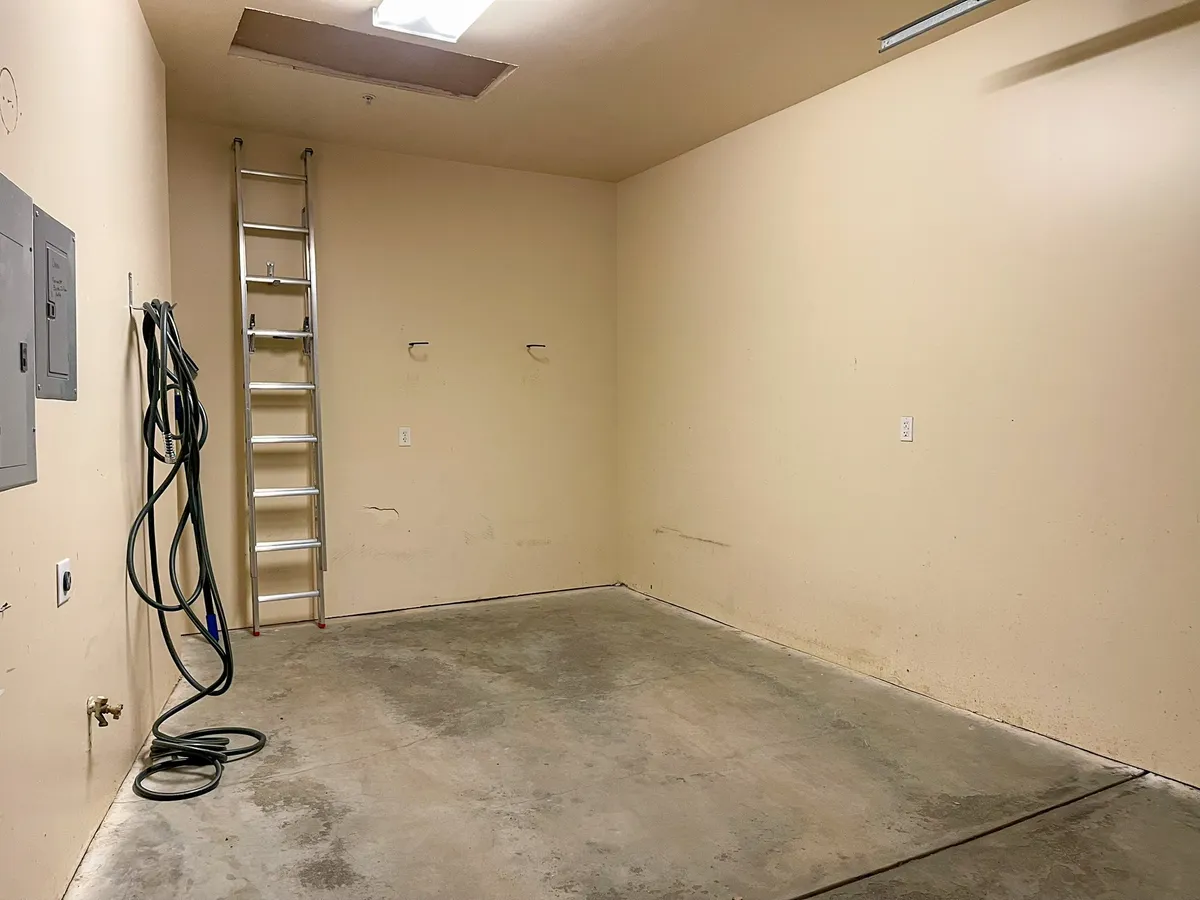 A functional garage interior space, showcasing storage solutions like a ladder, hose, and an electrical panel. The garage is tidy and organized, suggesting ample space for bikes, skis, and other gear.