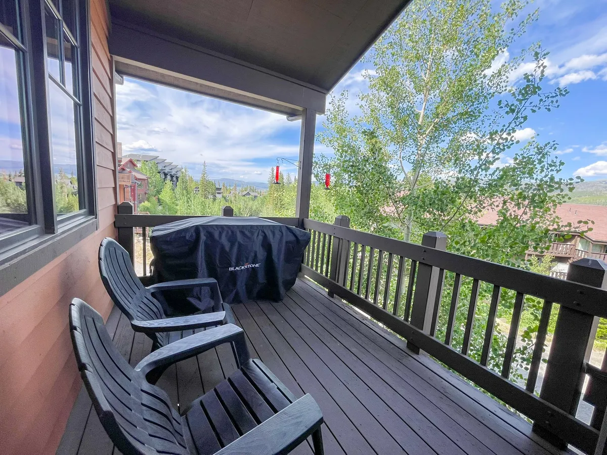 A peaceful deck scene with two black chairs facing lush green trees and the distant mountain view, accompanied by a grill. The atmosphere is inviting and tranquil, ideal for enjoying morning coffee, sunset views, or stargazing.