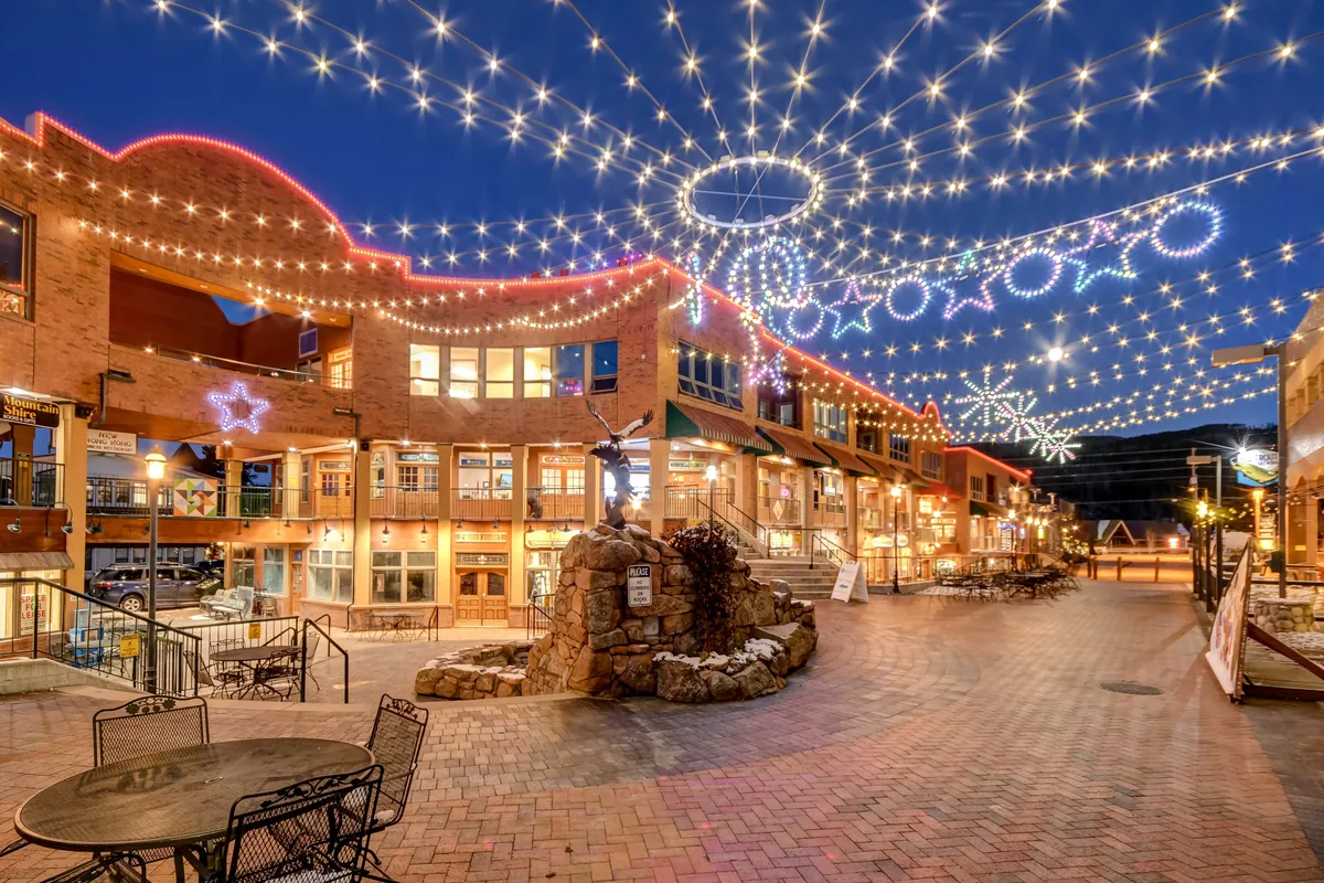 A festive exterior scene featuring twinkling string lights, decorative stars, and a central fountain, bustling with people enjoying shopping, dining, and socializing. The mood is joyful and energetic, capturing the essence of community events and seasonal celebrations.